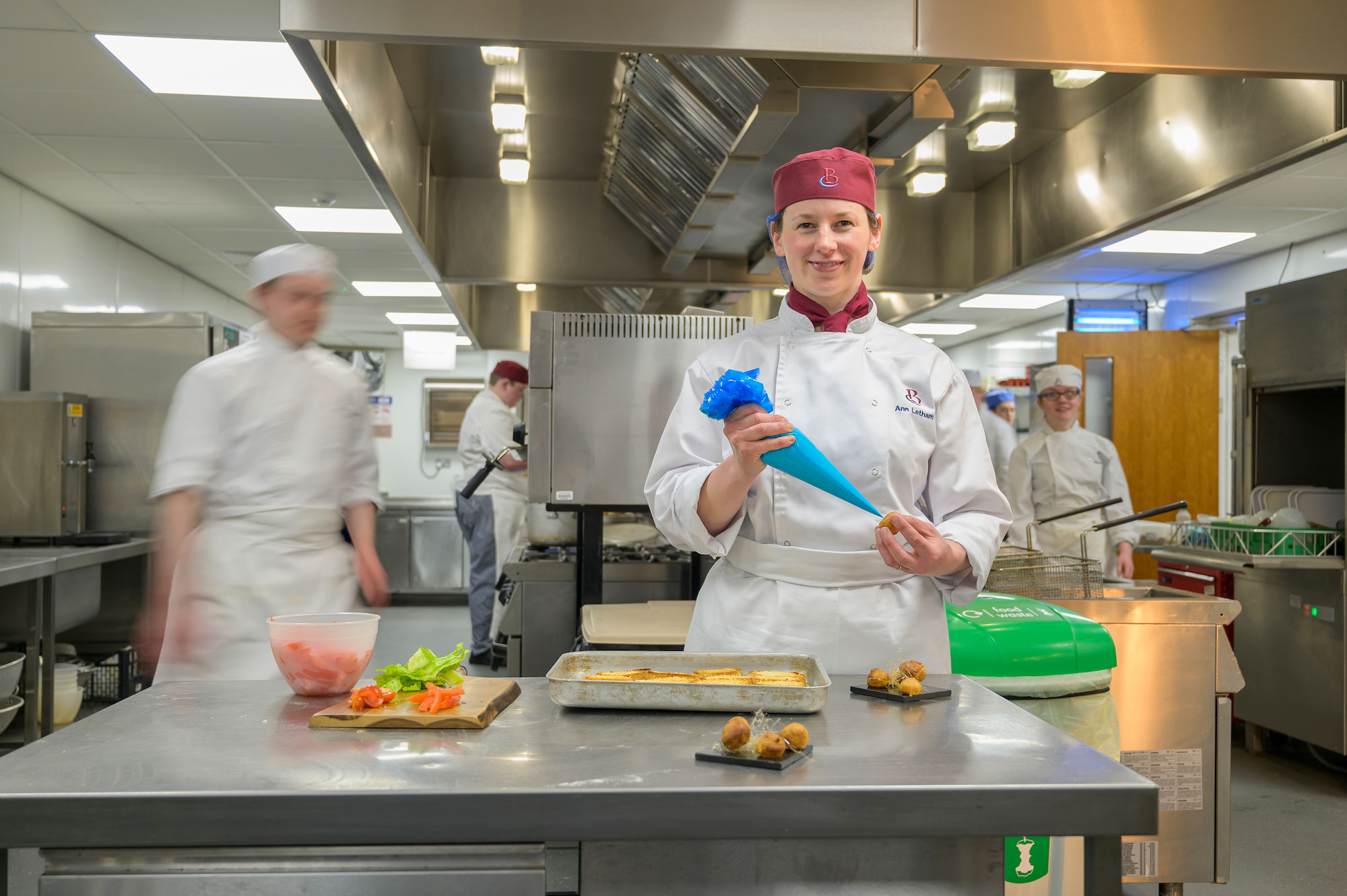 catering student stood in a kitchen, holding a piping bag