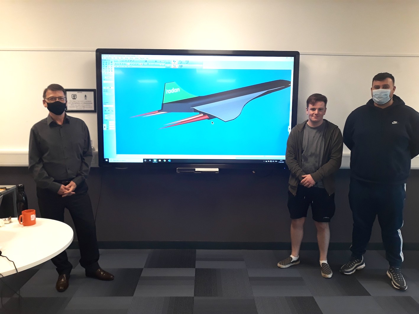 People standing next to large display monitor