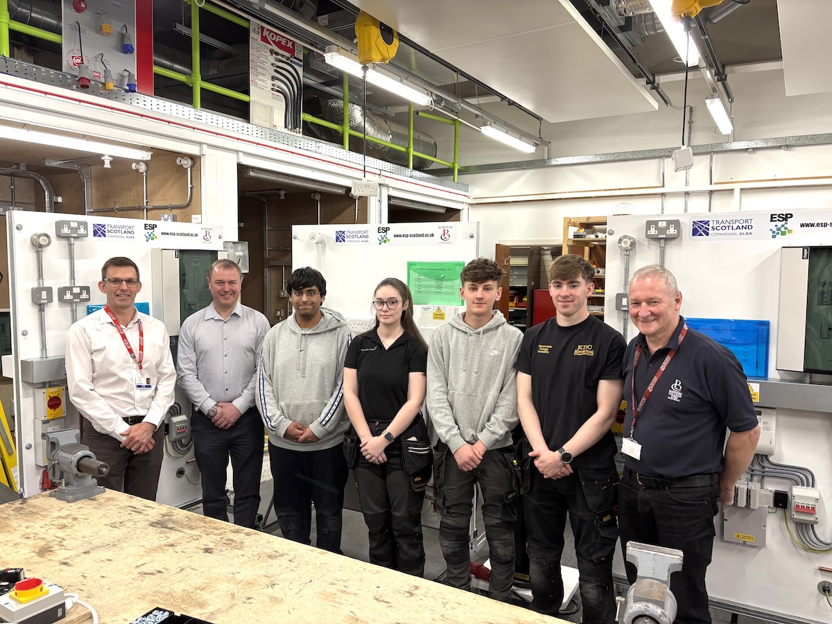 Group of staff and students standing in front of EV Rigs in an electrical workshop