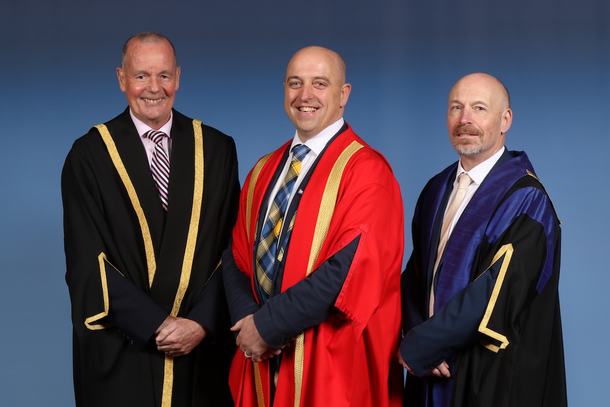 Official photograph of Chair of the Borders College Regional Board Ray McCowan, Honorary Fellow Bruce Aitchison, and Borders College Principal and CEO Pete Smith. All are pictured standing in front of a blue backdrop.