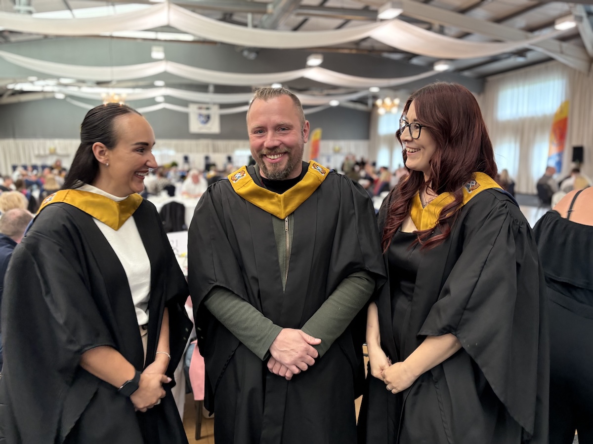 Three graduates pictured in a group photo wearing graduation gowns.
