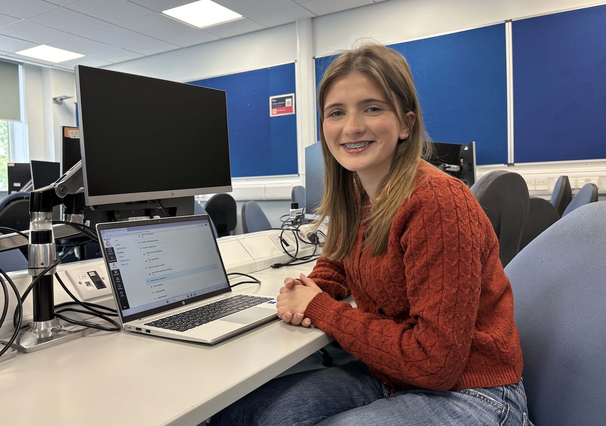 Photo of a students sitting in a classroom in front of a desktop computer