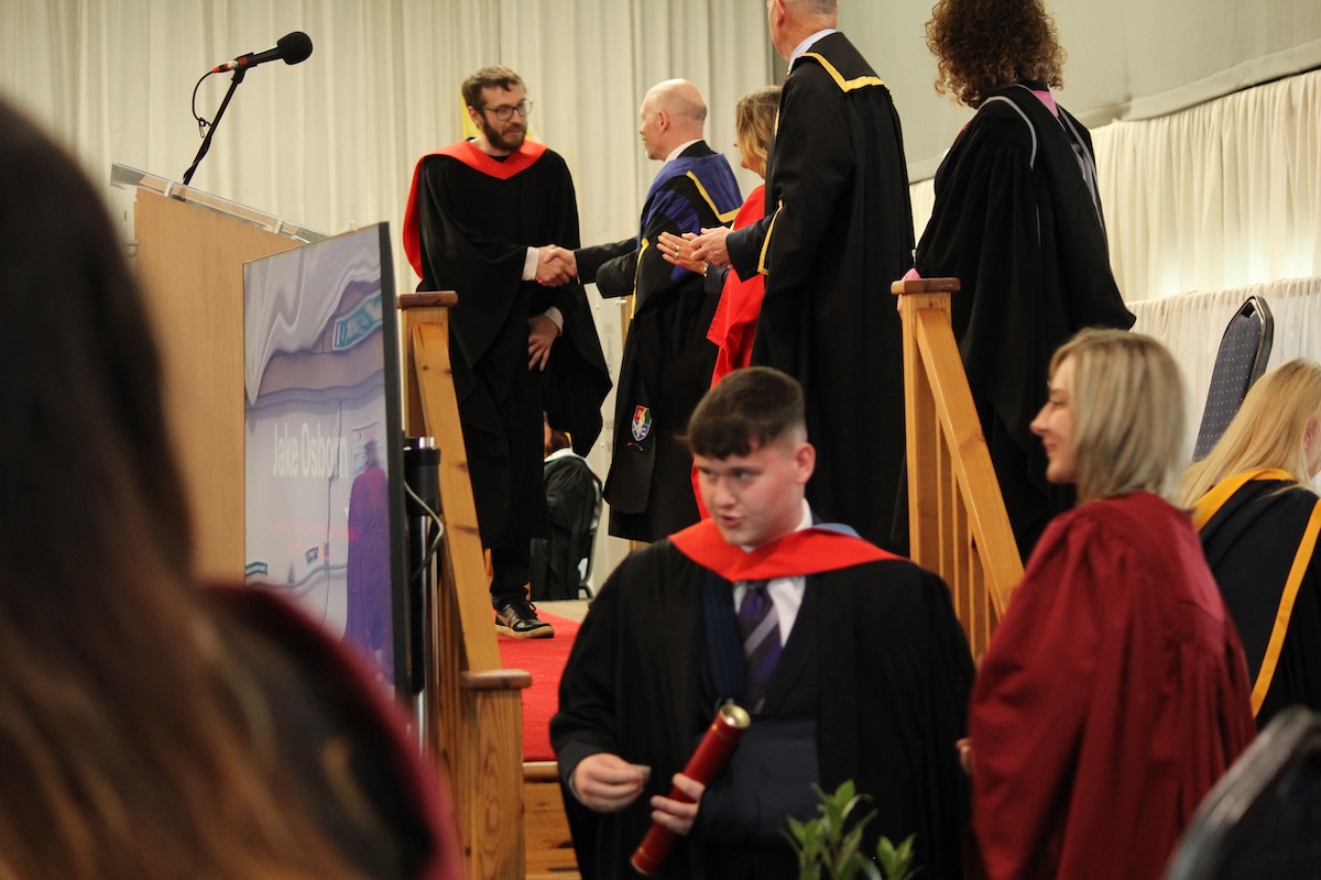 College staff presenting certificates to graduates on stage