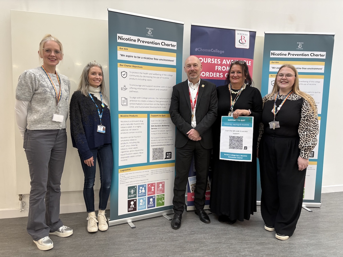 A group of 5 people standing at Borders College reception next to a nicotine prevention charter pull up board 